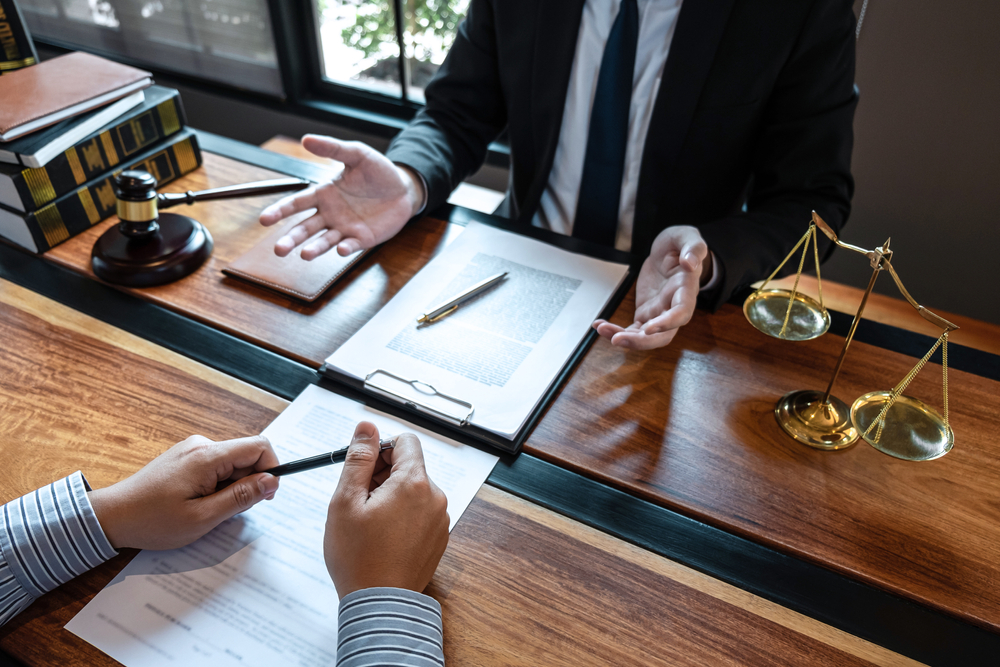 A professional male lawyer discussing a legal case negotiation with a client, reviewing contract documents in an office.